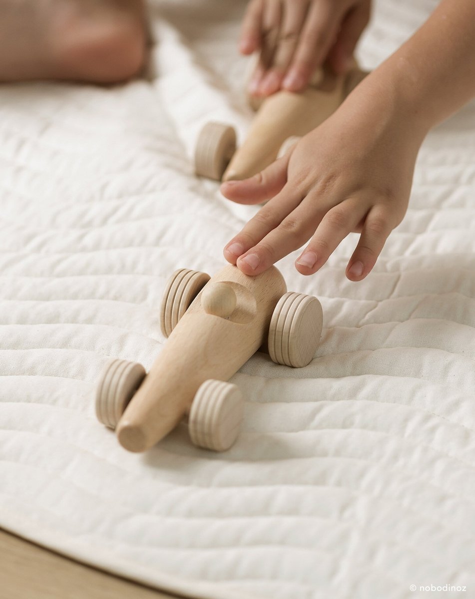 Nobodinoz Wooden Racing Car - Beech Wood, a child pushing the car on a mat